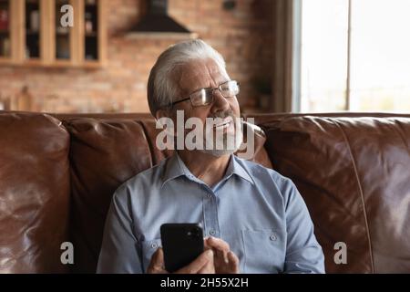 Un vieil homme attentionné s'assoit sur le canapé et regarde le téléphone de côté Banque D'Images