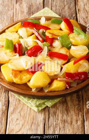 Pommes de terre frites avec oignons et poivrons rouges et verts dans une assiette sur la table. Vertical Banque D'Images