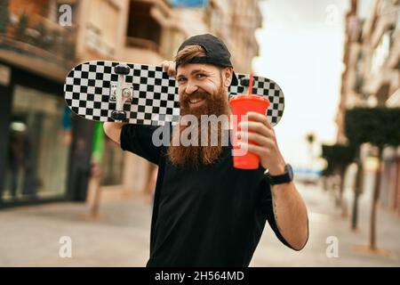 Jeune patineur irlandais tenant du skate et buvant du soda à la ville. Banque D'Images