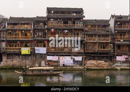 Hunan, Chine, 14 novembre 2011 : un bateau en bois navigue devant des maisons historiques le long de la rivière. Banque D'Images