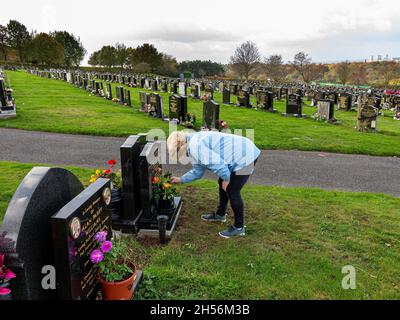 Une dame mûre met des roses sur une tombe un jour venteux Banque D'Images