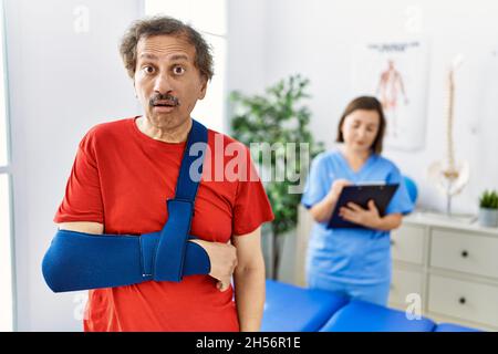 Homme d'asie du Sud-est portant le bras sur le harnais à la clinique de réadaptation peur et stupéfait avec la bouche ouverte pour la surprise, incrédulité visage Banque D'Images