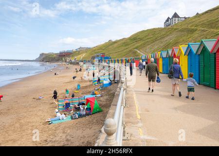Vacanciers sur la plage devant une rangée colorée de cabanes de plage sur le front de mer de Whitby North Yorkshire UK Banque D'Images