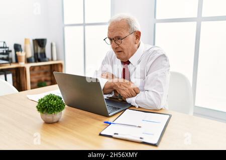 Homme âgé travaillant au bureau en utilisant un ordinateur portable qui a l'air endormi et fatigué, épuisé pour la fatigue et la gueule de bois, les yeux paresseux le matin. Banque D'Images