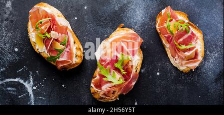 Sandwichs ouverts avec jamon, arugula et fromage dur sur fond de béton sombre.Style RUSTIK.vue de dessus. Banque D'Images