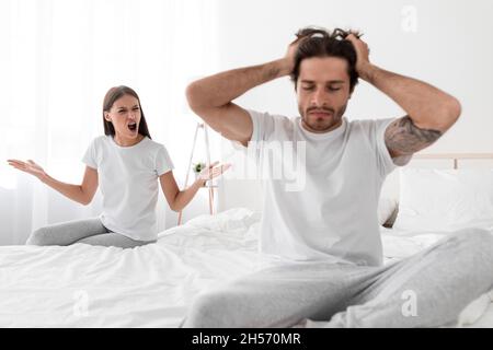 Triste mari européen millénaire avec le chaume est assis sur le lit et tient la tête avec la main, la femme se gonfle et hurle à Guy Banque D'Images