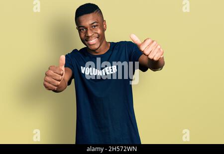 Jeune africain américain portant t shirt volontaire approuvant faire un geste positif avec la main, pouces vers le haut souriant et heureux pour le succès. Le vainqueur gestu Banque D'Images