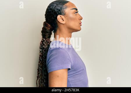 Homme hispanique portant un maquillage et des cheveux longs portant un t-shirt décontracté regardant à côté, détendez-vous posture avec visage naturel avec un sourire confiant. Banque D'Images