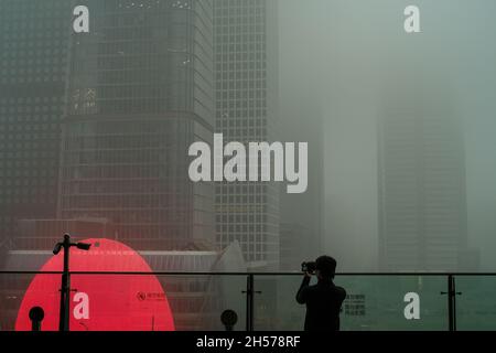 Un jeune homme photographie un gratte-ciel couvert de smog sévère dans le centre d'affaires de Beijing, en Chine.06 novembre 2021 Banque D'Images