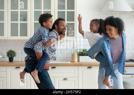 Heureux parents africains actifs coggydorant enfants frères, courant dans la cuisine Banque D'Images