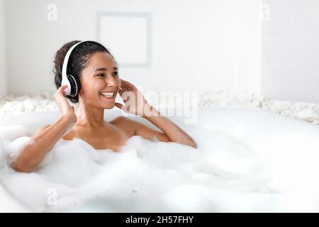 Bonne jeune femme dans un casque se détendre dans un bain moussant, écouter de la musique à la maison, l'espace libre Banque D'Images