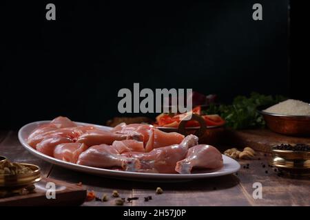 Poulet cru biriyani coupé sans peau disposé sur table blanche avec des ingrédients placés dans le fond avec le bois rustique fond. Banque D'Images