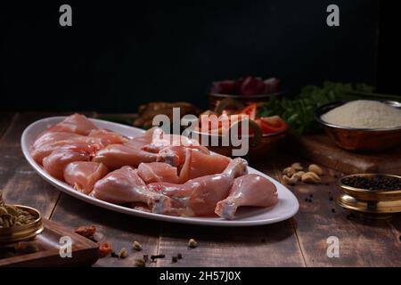 Poulet cru biriyani coupé sans peau disposé sur table blanche avec des ingrédients placés dans le fond avec le bois rustique fond. Banque D'Images