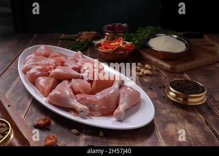 Poulet cru biriyani coupé sans peau disposé sur table blanche avec des ingrédients placés dans le fond avec le bois rustique fond. Banque D'Images