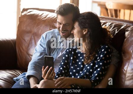 Un jeune couple surjoyeux se blottissez sur un canapé-lit, regardez la comédie sur le cellulaire Banque D'Images