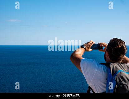 Le jeune homme du caucase prend une photo avec son smartphone à la mer Banque D'Images
