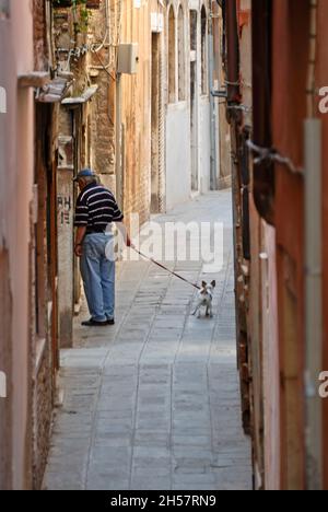 Un homme méconnaissable marche avec son chien à travers la ville de Venise, en Italie. Banque D'Images