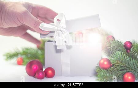 Boîte cadeau ouverte à la main à Noël. Décorations rouges de boules de Noël et branches de sapin ou de pin. Banque D'Images