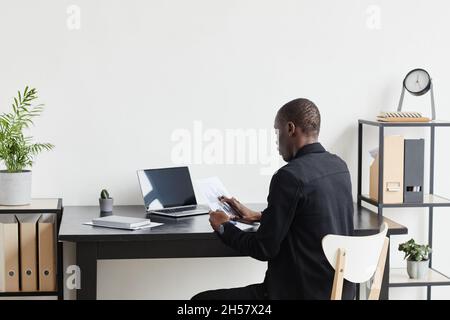 Portrait de l'homme d'affaires afro-américain travaillant par bureau à domicile, espace de copie, avec une vue arrière minimale Banque D'Images