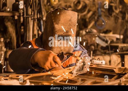 Un soudeur industriel dans un écran de protection est engagé dans des travaux de soudage et de réparation de la porte de voiture dans l'atelier de l'usine. Banque D'Images