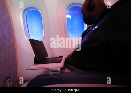 Un homme noir assis dans un siège d'avion portant un masque qui regarde la fenêtre avec un iPad Banque D'Images