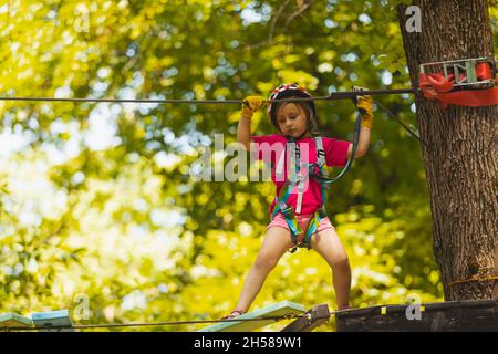 La jeune fille concentrée surmonte soigneusement les obstacles dans le parc de corde Banque D'Images