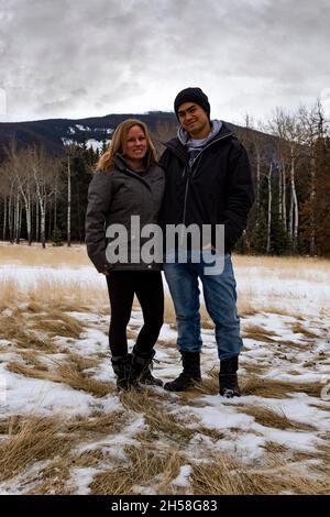 Couple posant devant la ligne d'arbre le jour sombre couvert en hiver. Petite quantité de neige, herbe morte.Montagne en arrière-plan Banque D'Images