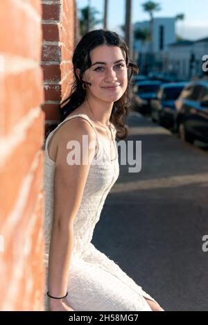 Confiante école secondaire fille assise dans le bâtiment rustique de brique fenêtre sil avec la lumière du soleil dorée shiniing sur elle. Banque D'Images