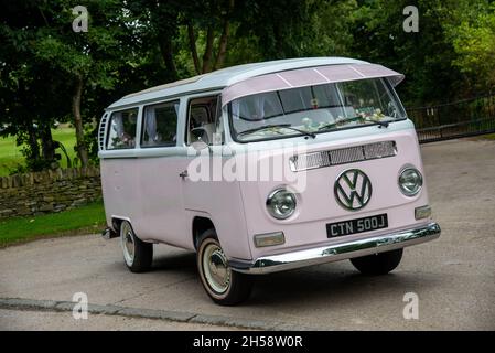 Mariage rose Volkswagen campeur Van 'Bay Window' garé sur une voie de campagne avec arbres et champs derrière Banque D'Images