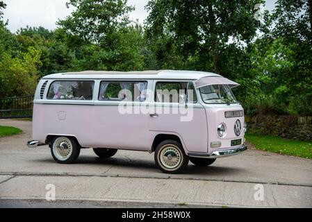 Mariage rose Volkswagen campeur Van 'Bay Window' garé sur une voie de campagne avec arbres et champs derrière Banque D'Images