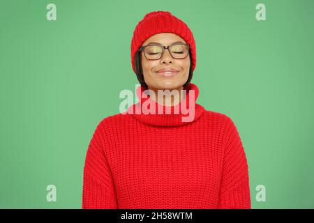 Femme africaine insouciante en chandail chaud et chapeau tricoté sourire avec les yeux fermés semble heureux et calme Banque D'Images