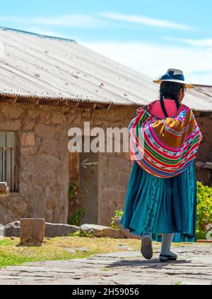 Femme autochtone péruvienne quechua vêtue de vêtements traditionnels marchant dans une rue de l'île Taquile près du lac Titicaca, Pérou. Banque D'Images