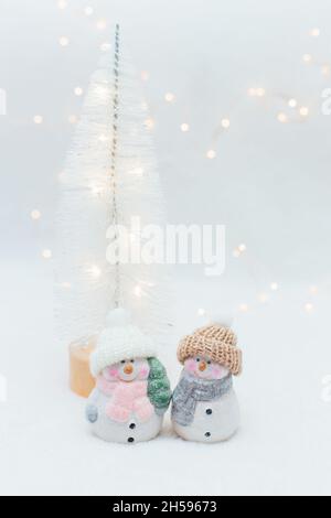 Figurines décoratives sur le thème de Noël.Deux statuettes d'un bonhomme de neige dans un chapeau tricoté sur fond blanc.Décoration festive, lumières bokeh chaleureuses Banque D'Images