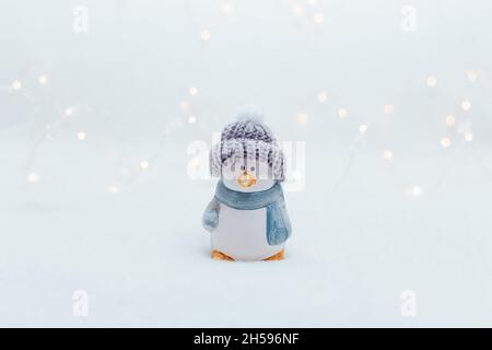 Figurines décoratives sur le thème de Noël.La statuette d'un pingouin dans un bonnet tricoté sur fond blanc.Décoration festive, lumières bokeh chaleureuses Banque D'Images