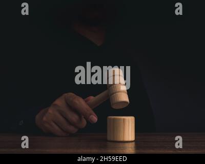 Un juge en bois Gavel à la main avec la table de son sur une table en bois sur fond sombre.Homme en chemise noire frappant le jouet de marteau en bois, Justice, loi Banque D'Images