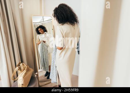 Jeune femme élégante dans les cabines d'essayage regardant le miroir essayer de nouveaux vêtements Banque D'Images