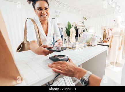 Un client satisfait qui paie par téléphone intelligent à un comptoir dans un magasin de vêtements Banque D'Images