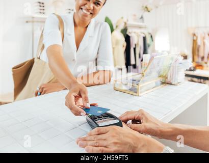 Femme élégante payant par carte de crédit à un comptoir dans un petit magasin de vêtements Banque D'Images