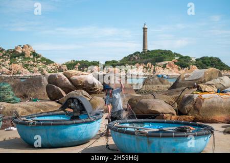 Un pêcheur local délite le filet de pêche sur le bord de mer.Plage pittoresque avec de grands rochers.Le vieux phare se trouve au loin.Haute qualité Banque D'Images