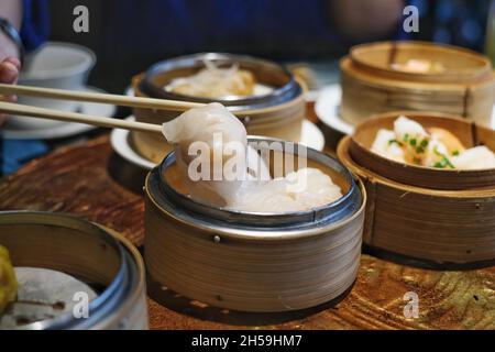 Une photo en gros plan de baguettes de bambou ramassant des boulettes chinoises blanches farcies à la vapeur, également connu sous le nom de dim sum d'un panier rond de bambou sur un Banque D'Images