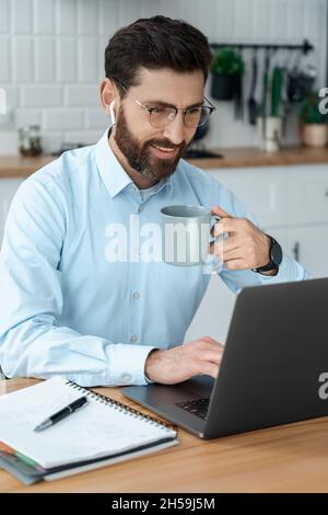 Homme d'affaires dans une chemise élégante devant un ordinateur portable regardant l'écran boire du café Banque D'Images