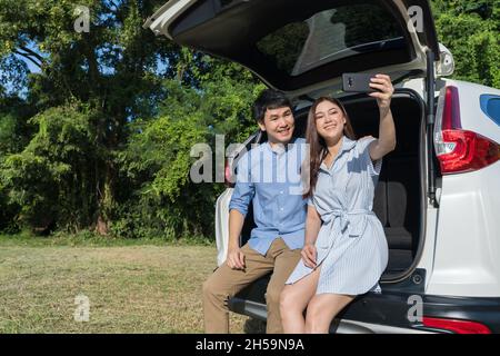 couple heureux amoureux assis et en utilisant un smartphone en train de prendre un selfie en voiture ouverte de retour Banque D'Images
