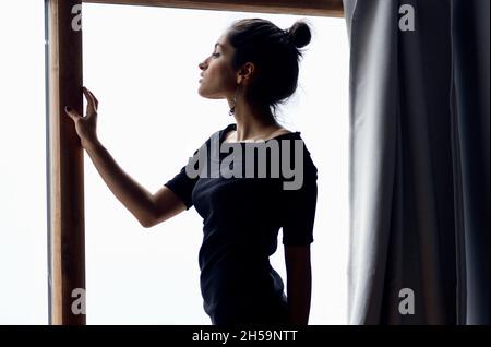 belle femme dans une robe noire près de la fenêtre posant style élégant Banque D'Images