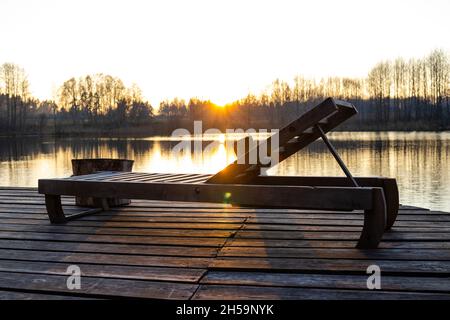 Un transat en bois se dresse sur un quai au bord du lac en automne.La saison touristique est terminée, l'automne est venu Banque D'Images