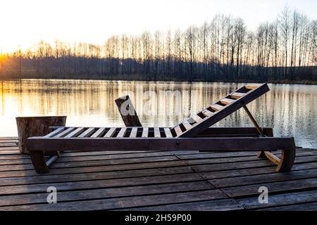 Un transat en bois se dresse sur un quai au bord du lac en automne.La saison touristique est terminée, l'automne est venu Banque D'Images