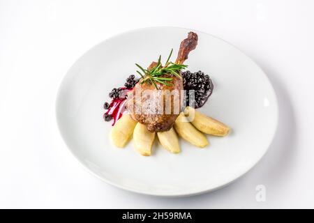 Cuisse de canard cuite avec des pommes et de la sauce au cassis sur une assiette blanche vue rapprochée d'en haut. Banque D'Images