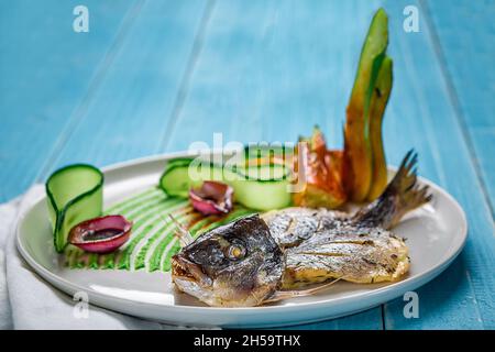 La friture de poissons dorado, décoré avec des concombres et oignons. Sur un fond de bois bleu Banque D'Images