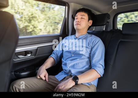 jeune homme dormant assis sur le siège arrière de la voiture Banque D'Images