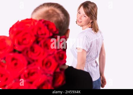 Blonde heureuse femme a tourné sa tête vers un liveur et le regardant avec un sourire et il tient le beau bouquet de roses derrière Banque D'Images