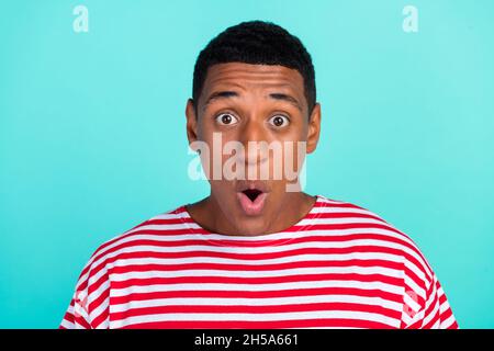 Photo de funky choqué jeune homme porter t-shirt rayé grands yeux isolé teal couleur fond. Banque D'Images